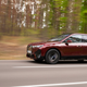 A photo of a burgundy BMW iX SUV driving on a tree-lined road.